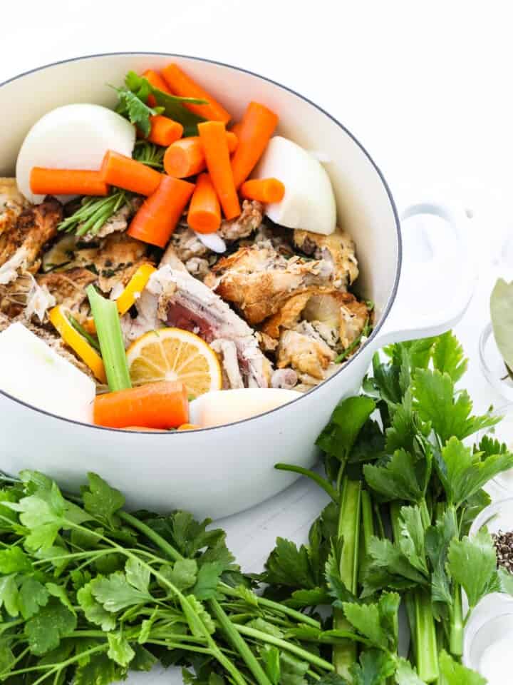 A large white cooking pot filled with ingredients to make chicken stock at home.