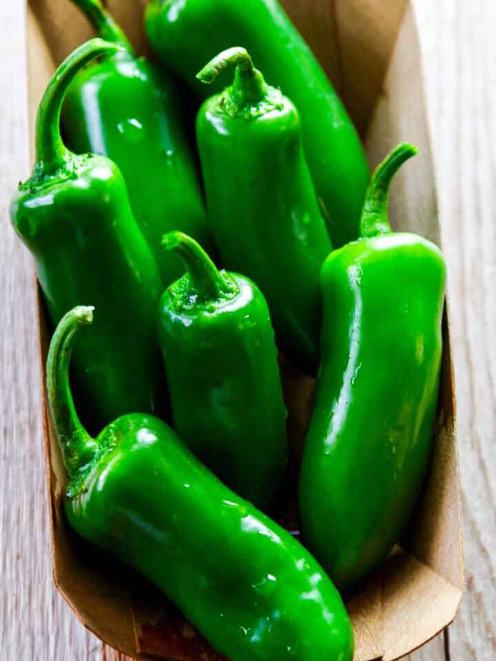 A small wooden container basket filled with bright green jalpaenos washed with water drops.