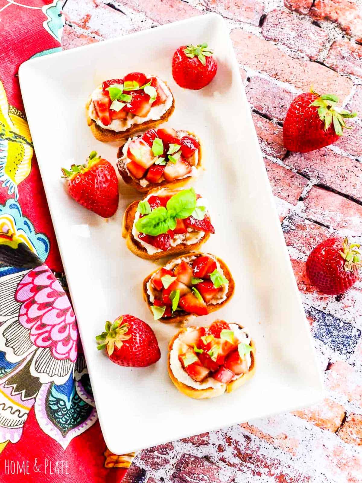 A white platter with strawberry topped crostini appetizer at a party.