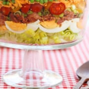 A glass trifle dish filled with 7 Layer Salad full of colorful ingredients.