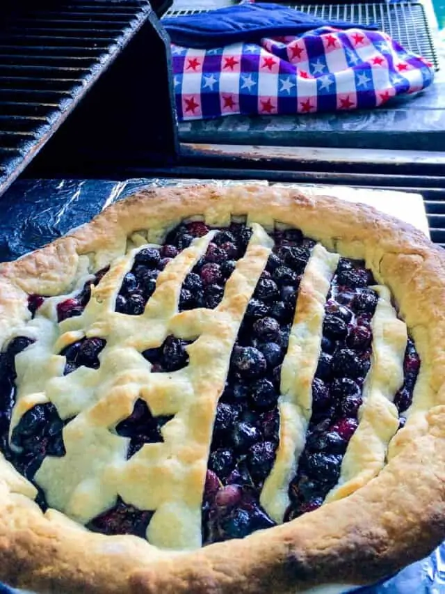 A blueberry pie that is baked outdoors on a grill with a flag shaped pie crust.