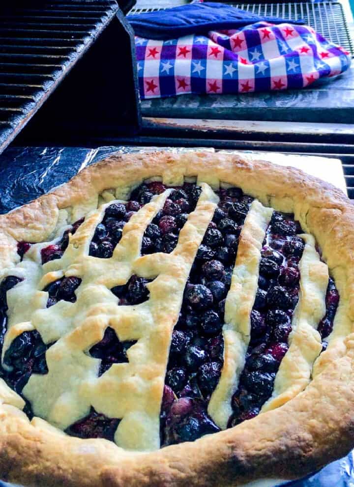 A blueberry pie that is baked outdoors on a grill with a flag shaped pie crust.