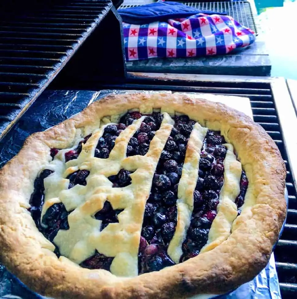 A blueberry pie that is baked outdoors on a grill with a flag shaped pie crust.