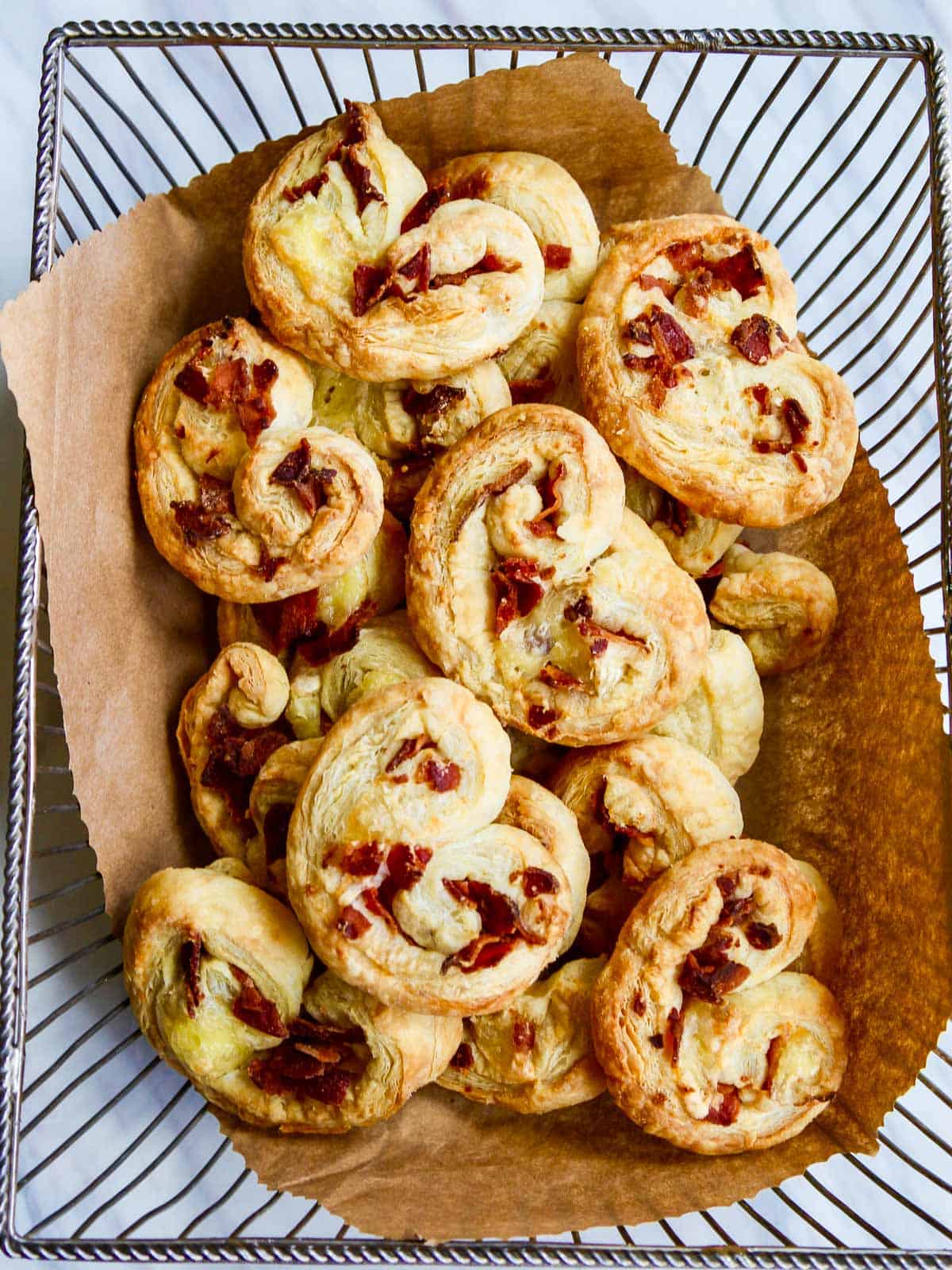 A vintage silver basket lined with brown parchment paper and filled with brie and bacon palmiers freshly baked from the oven.