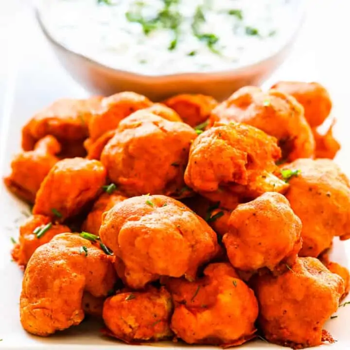 Baked Buffalo Cauliflower on a plate with ranch dip sprinkled with fresh herbs.