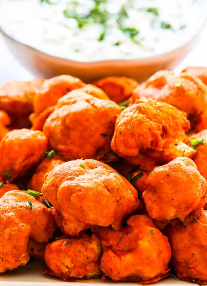 Baked Buffalo Cauliflower on a plate with ranch dip sprinkled with fresh herbs.