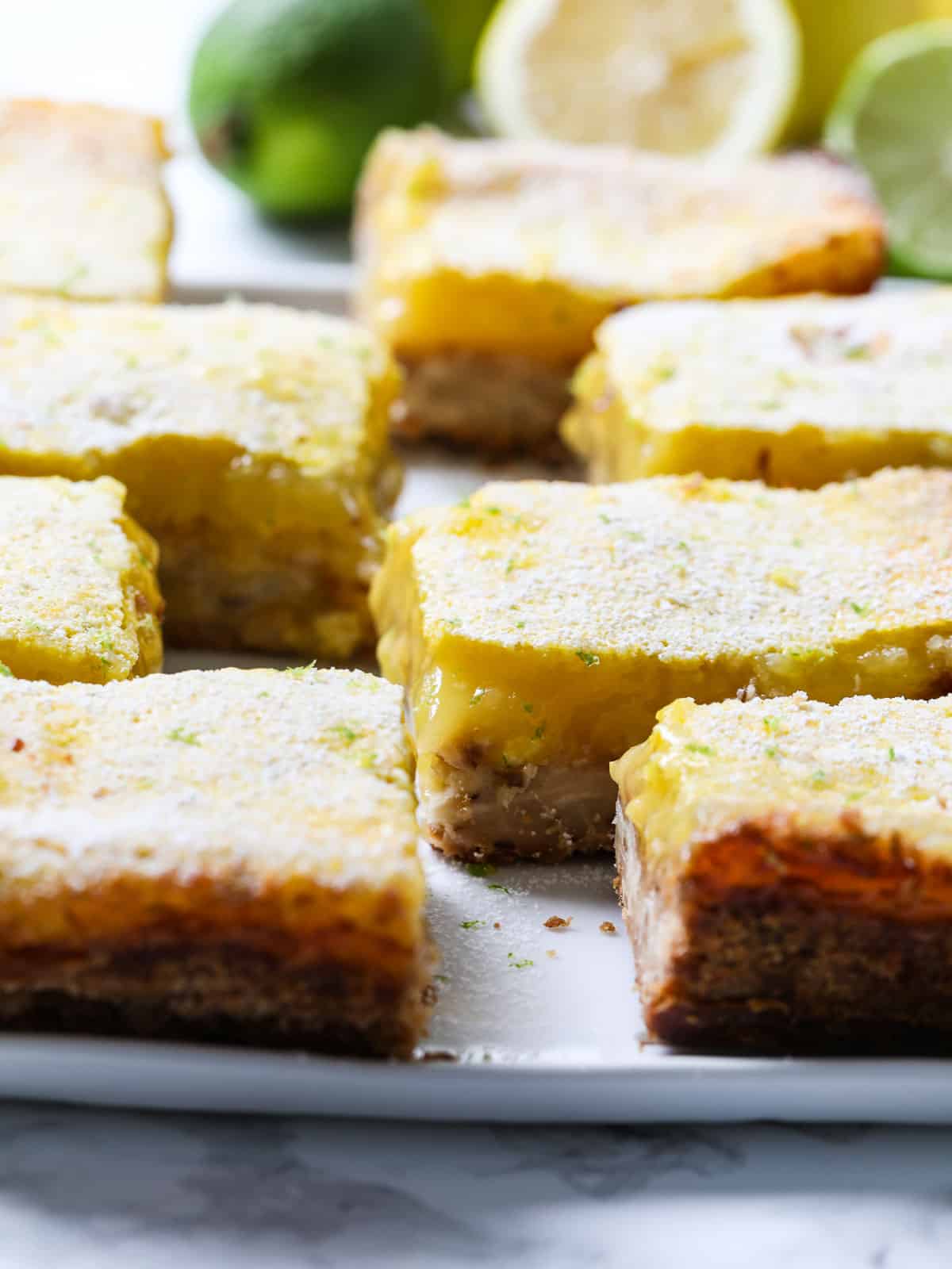 Large slice lemon bars dusted with powder sugar and lime zest on a white plate.