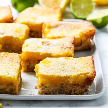 A white plate with large lemon bars cut into squares dusted with powder sugar.