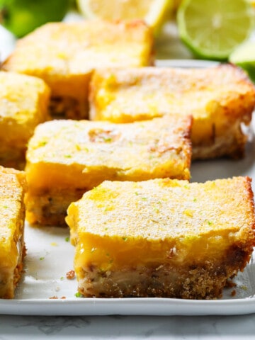 A white plate with large lemon bars cut into squares dusted with powder sugar.