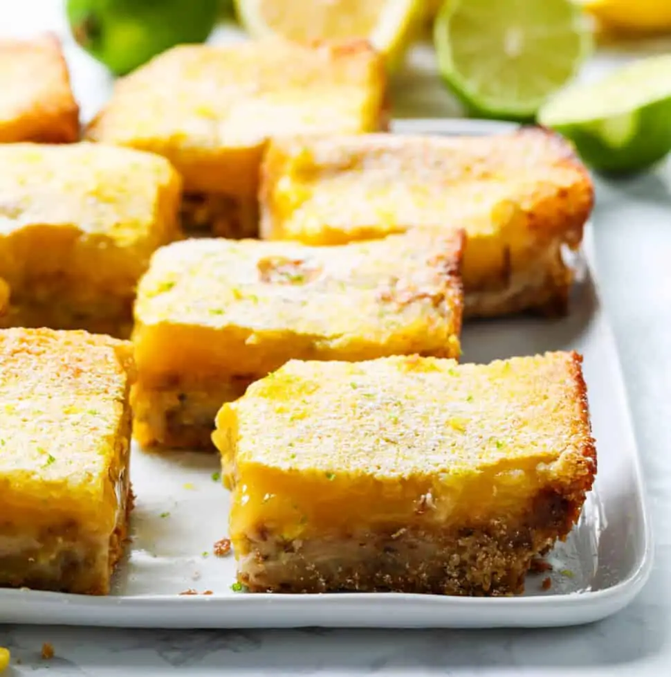 A white plate with large lemon bars cut into squares dusted with powder sugar.