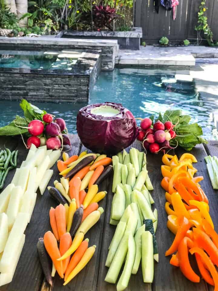 A board of crudites with dip by a blue swimming pool.
