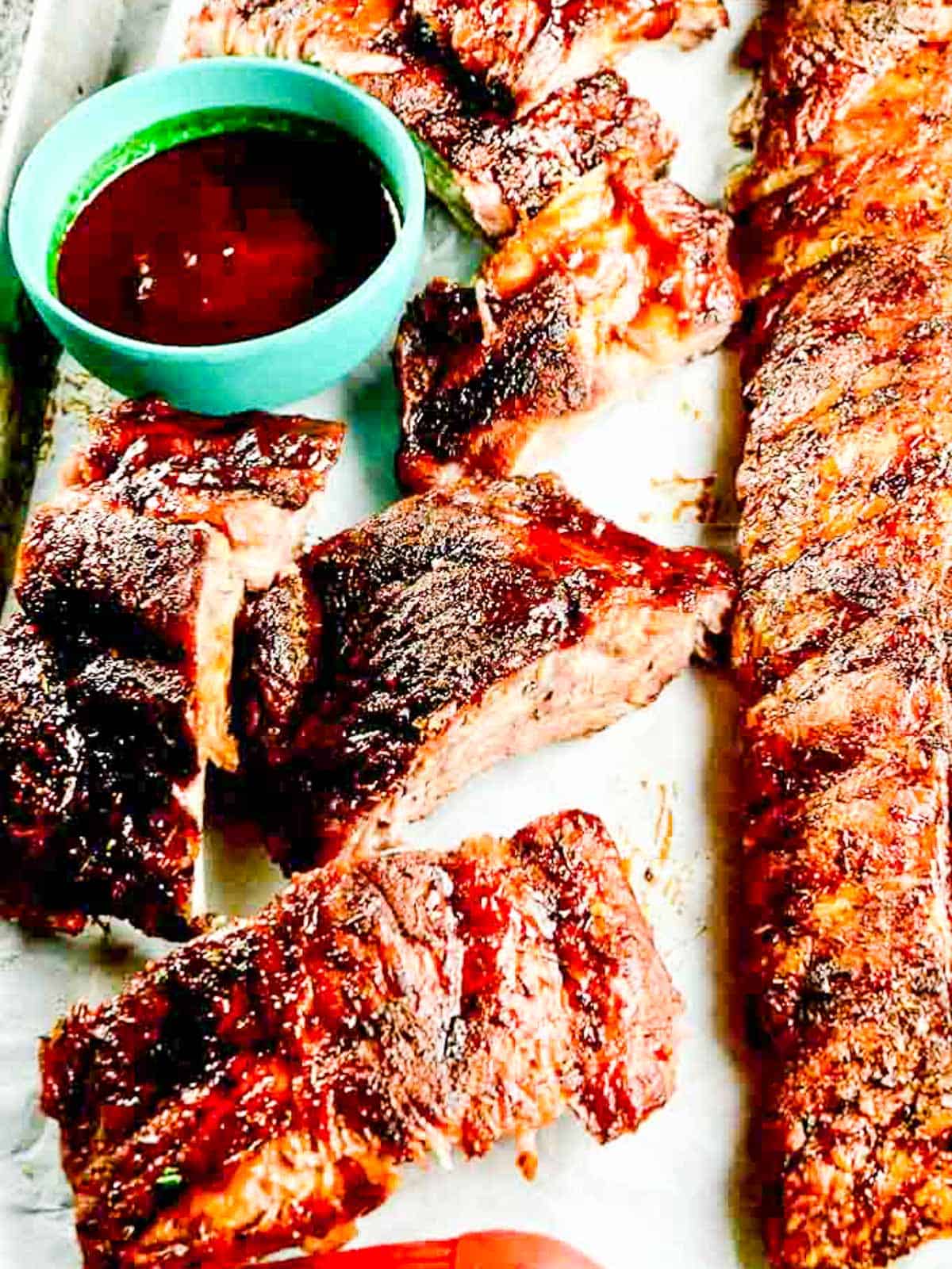 A platter filled with well seasoned BBQ ribs with BBQ sauce.