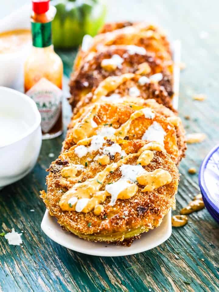 A white long plate with a stack of fried green tomatoes with remoulade and buttermilk ranch dressing.