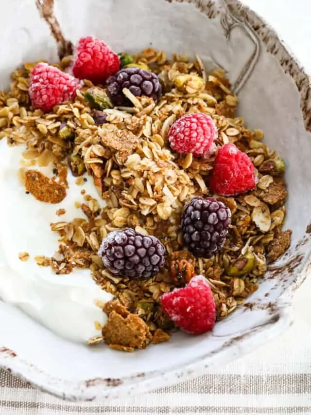 A handmade ceramic bowl filled with yogurt and topped with granola, raspberries, and black berries.