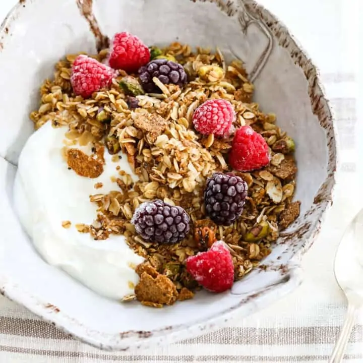 A handmade ceramic bowl filled with yogurt and topped with granola, raspberries, and black berries.
