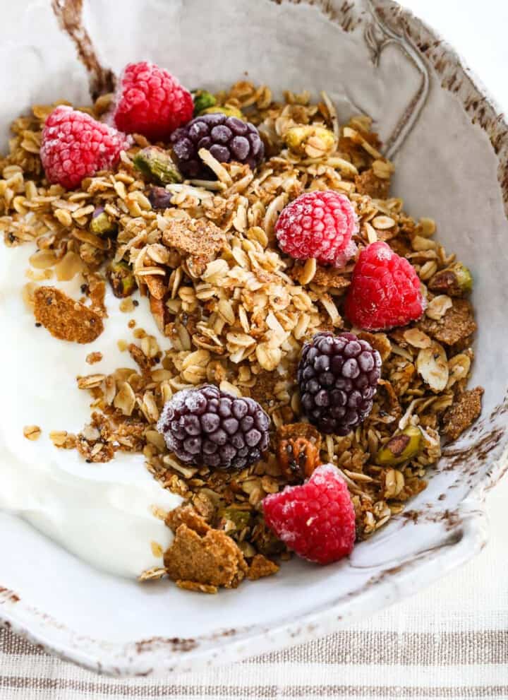 A handmade ceramic bowl filled with yogurt and topped with granola, raspberries, and black berries.