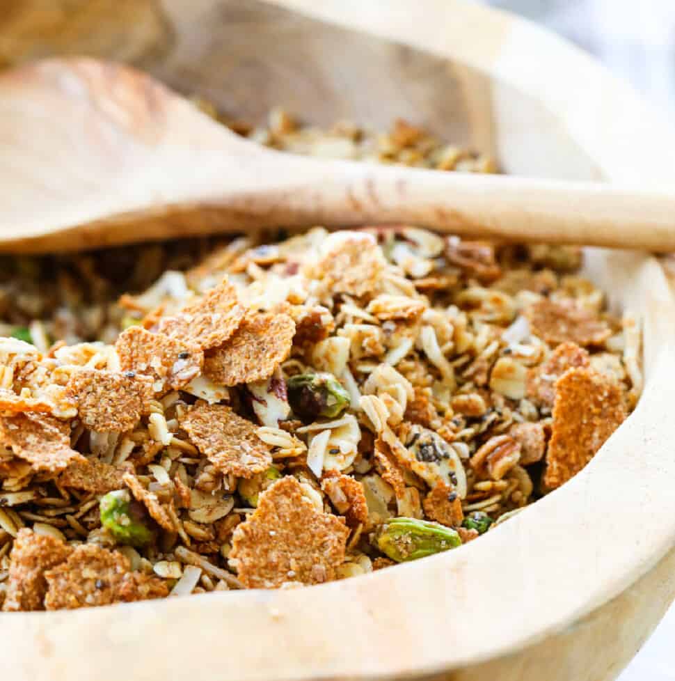 A wooden bowl filled with granola and a wooden spoon.