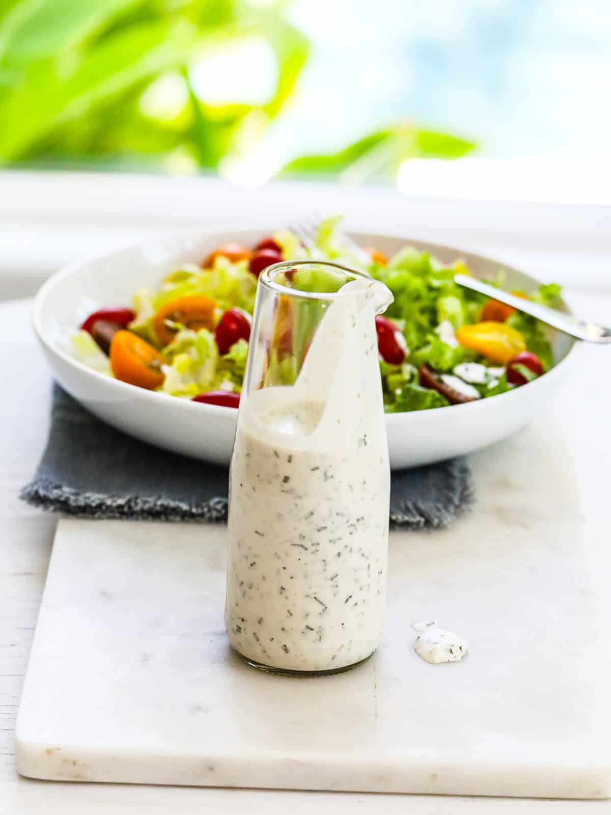 A white low bowl of colorful salad with ranch dressing in a glass carafe.