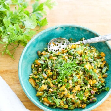 A blue vintage bowl filled with chopped Gremolata with a silver spoon.