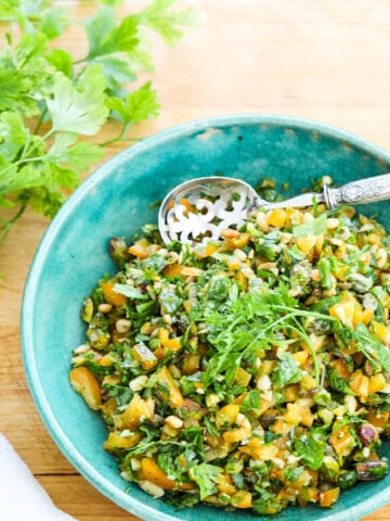 A blue vintage bowl filled with chopped Gremolata with a silver spoon.