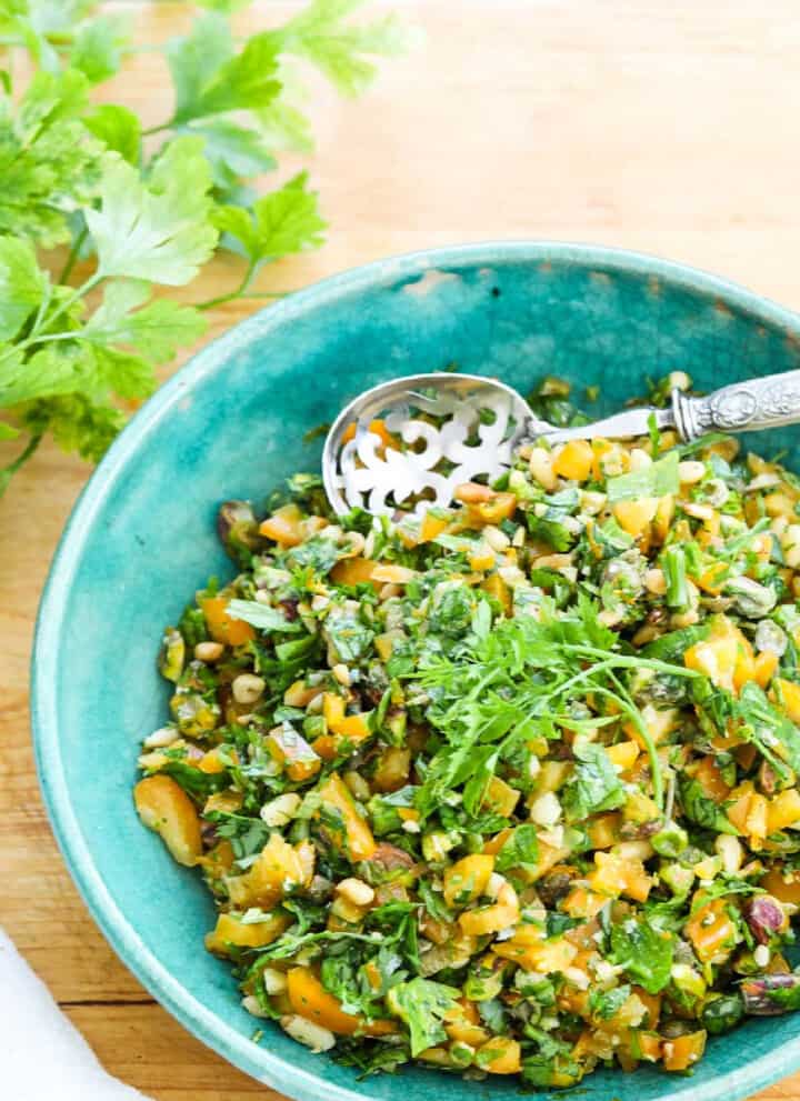 A blue vintage bowl filled with chopped Gremolata with a silver spoon.