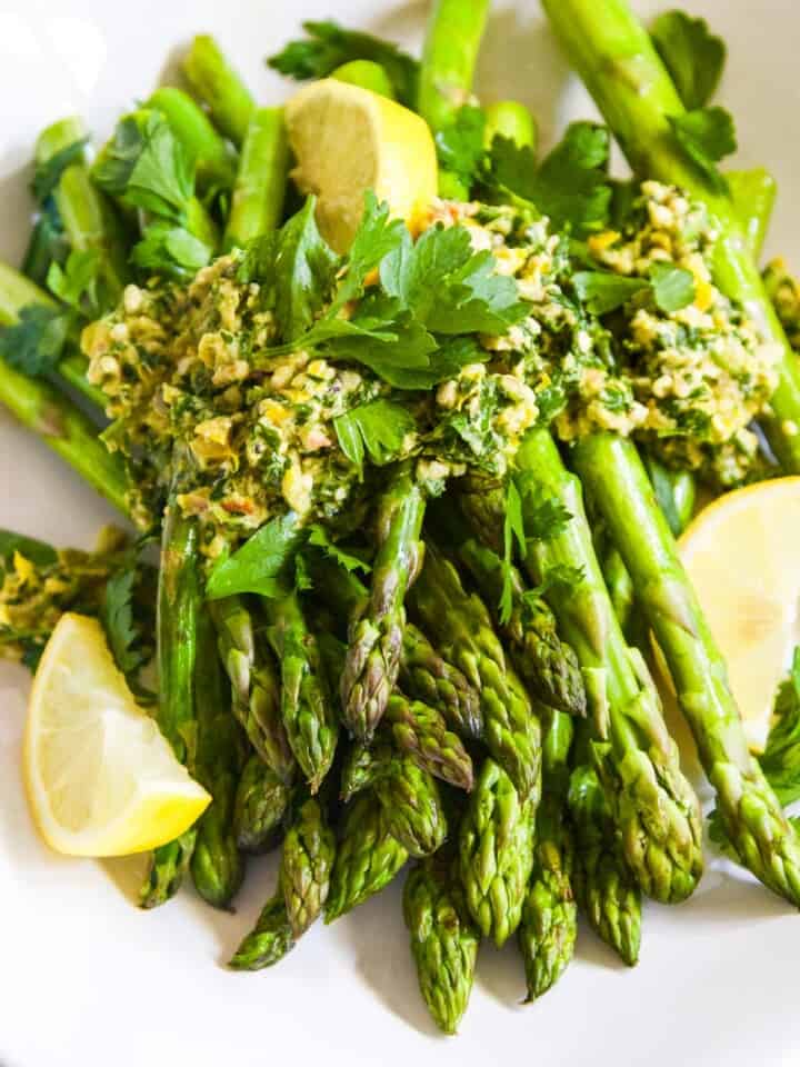 A large white plate filled with sauteed asparagus and topped with gremolata garnished with lemons.