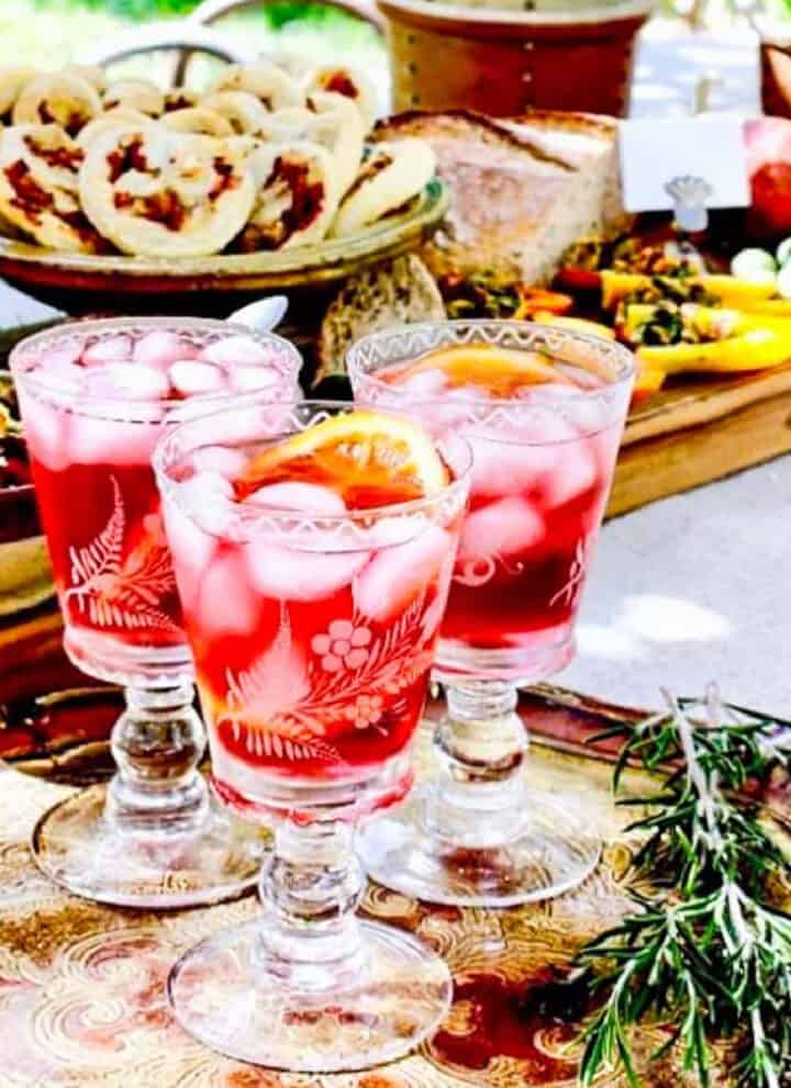 A decorative etched cocktail glass with a red hibiscus keto cocktails garnished with an orange slice.