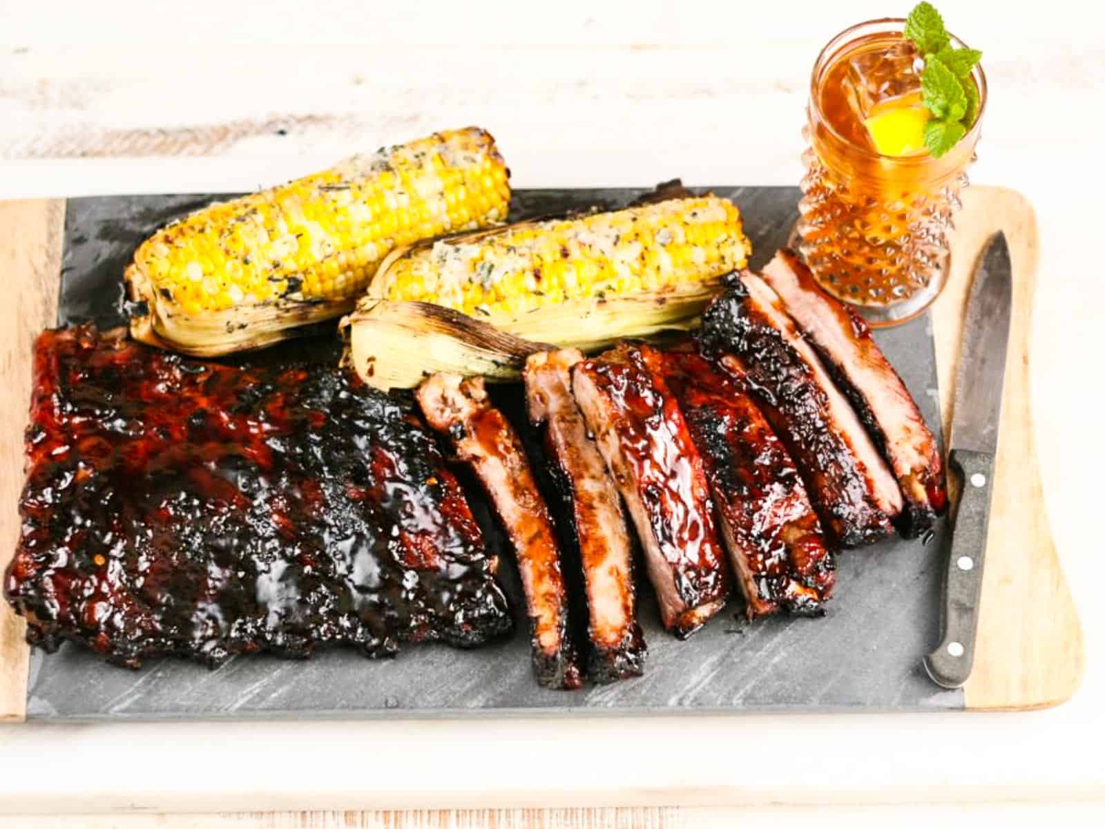 A pile of BBQ ribs with corn and sweet tea at a BBQ cookout.