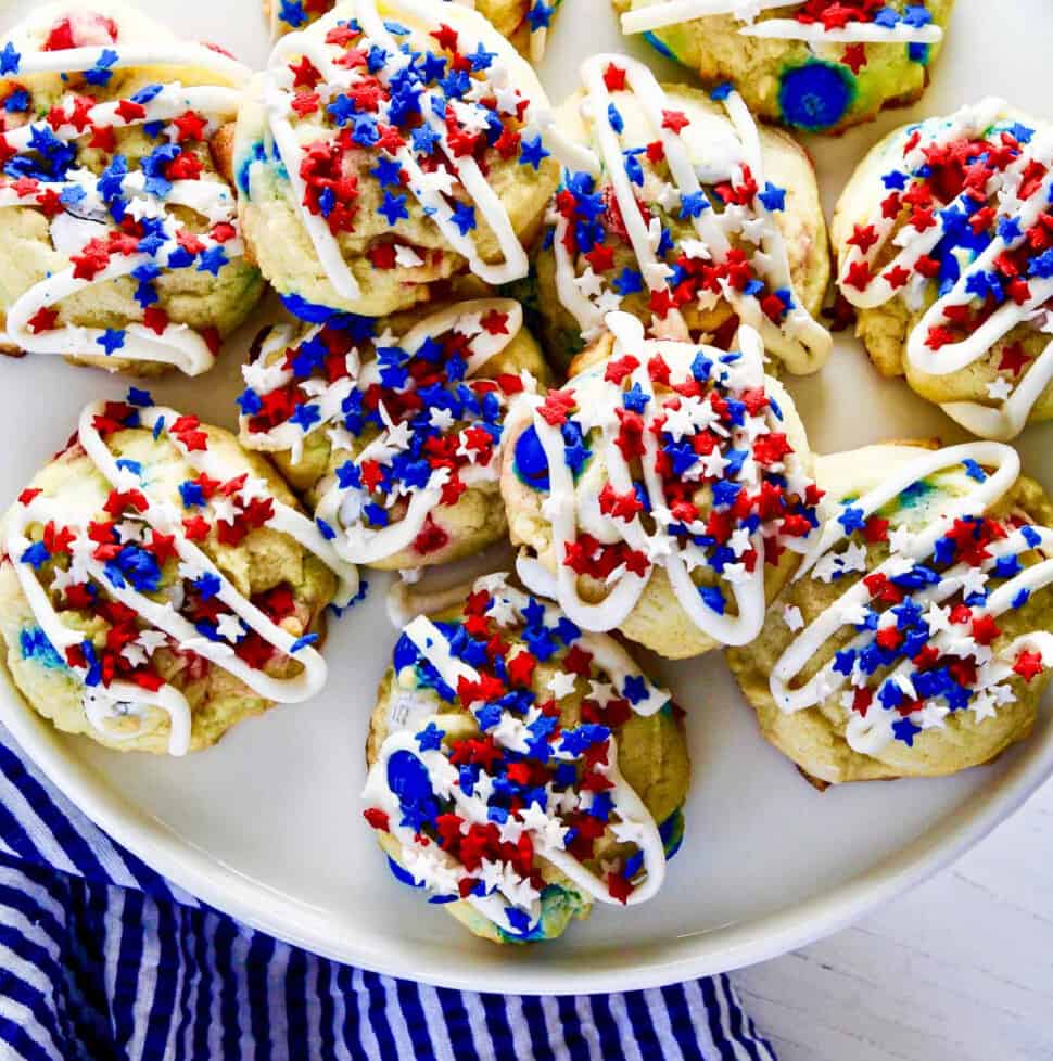 A white plate filled with July 4th red white and blue cookies with icing and star sprinkles.