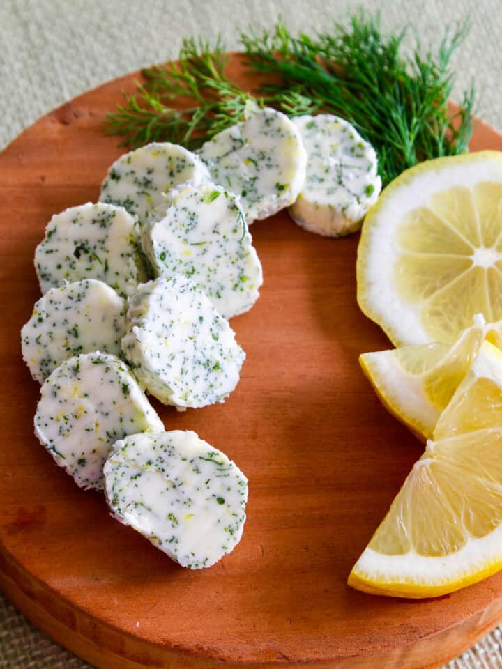 A small round cutting board with slices of lemon dill butter and sliced lemon garnish.