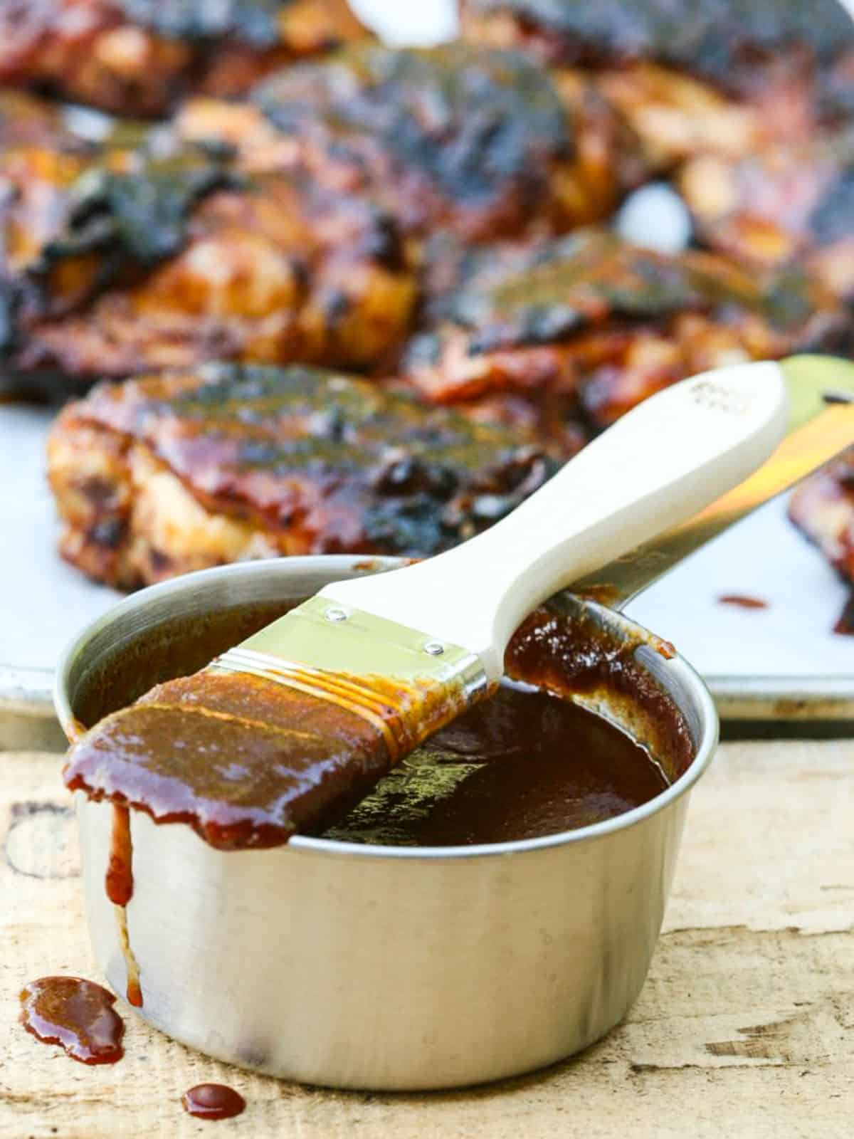 A silver container filled with bbq sauce, and a brush dripping with the sauce.