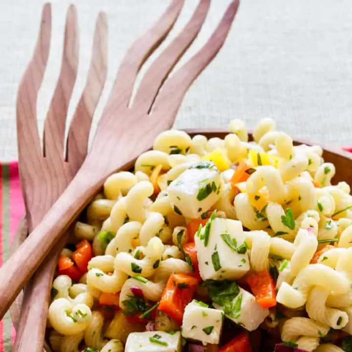A wooden bowl filled with pasta salad and wooden serving tongs.