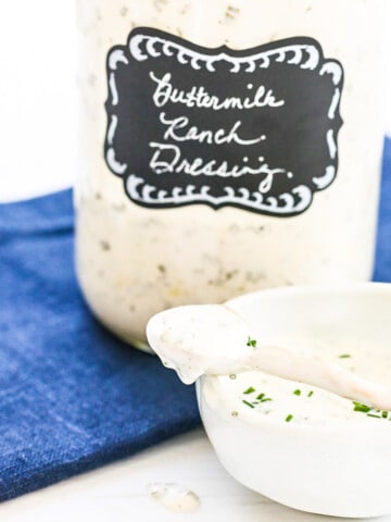 A large Mason jar filled with ranch dressing made at home with a small serving bowl and spoon.