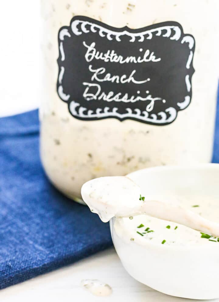 A large Mason jar filled with ranch dressing made at home with a small serving bowl and spoon.