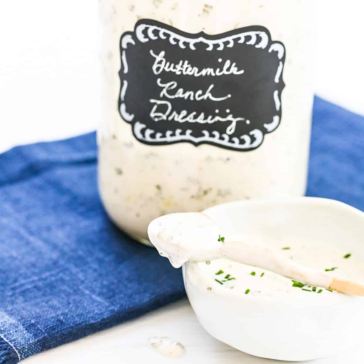 A large Mason jar filled with ranch dressing made at home with a small serving bowl and spoon.