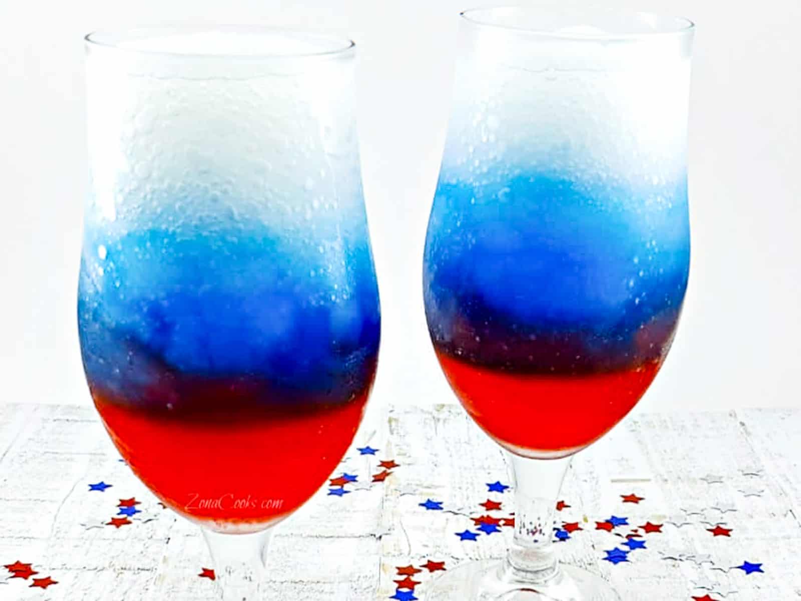 Two glasses of red white and blue drinks on ice in wine goblets.