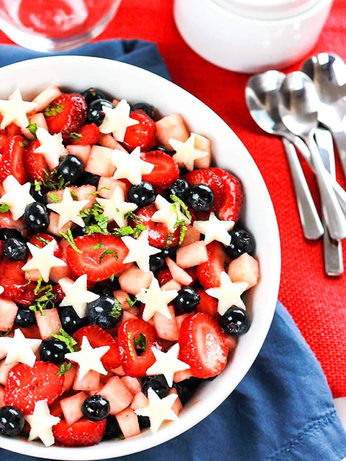 A white bowl filled with salad made with strawberries, blueberries and jicama stars.