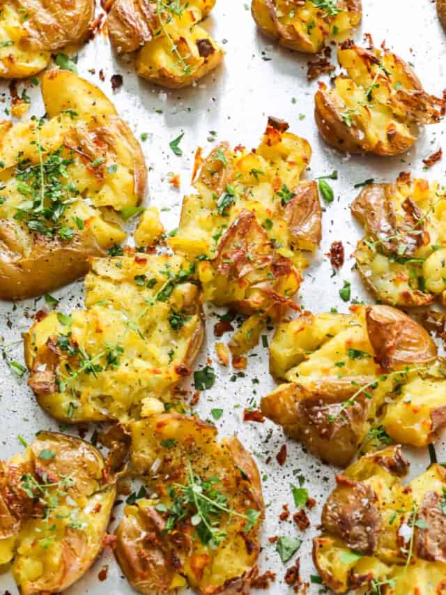 A sheet pan of smashed potatoes with fresh herbs baked with crispy golden brown edges.