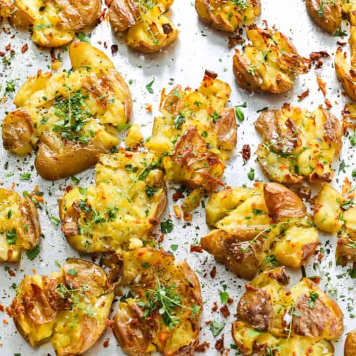 A sheet pan of smashed potatoes with fresh herbs baked with crispy golden brown edges.