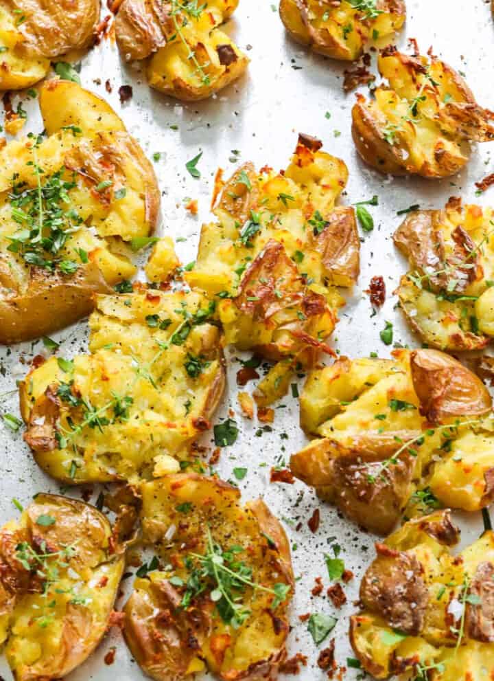 A sheet pan of smashed potatoes with fresh herbs baked with crispy golden brown edges.