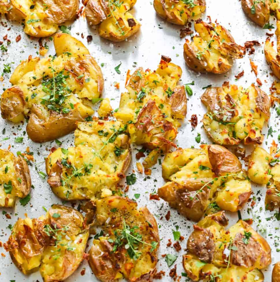 A sheet pan of smashed potatoes with fresh herbs baked with crispy golden brown edges.