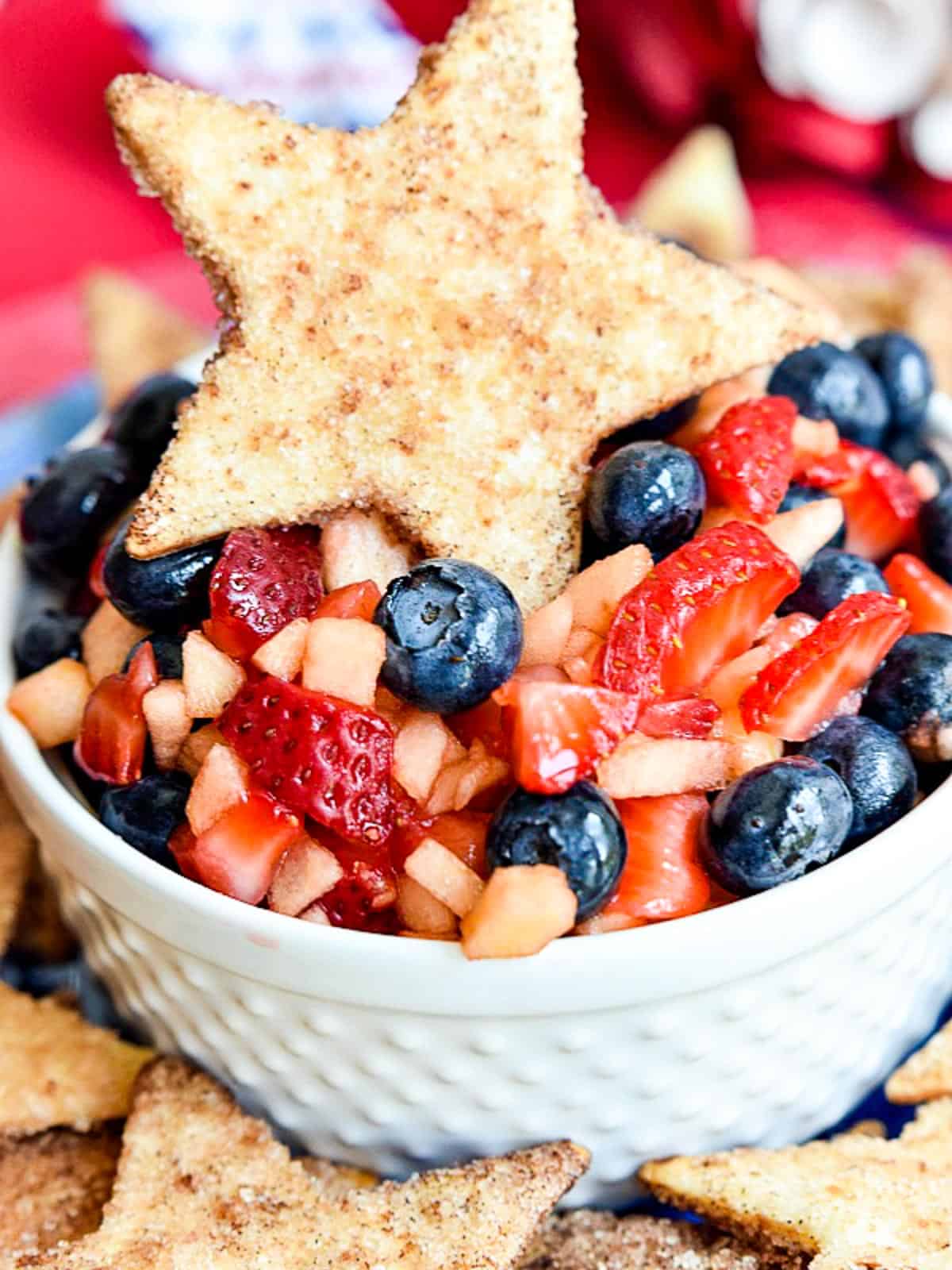 A white bowl with fruit salsa and a cinnamon cookie on top.