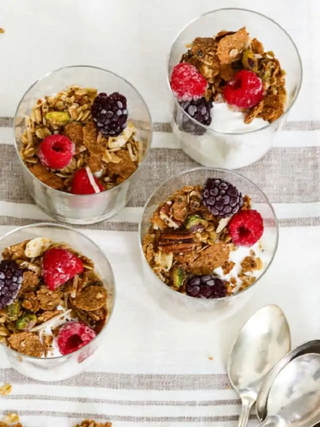 Four small yogurt parfaits made with yogurt, granola and berries.