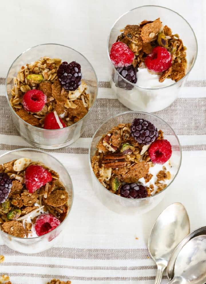 Four small yogurt parfaits made with yogurt, granola and berries.