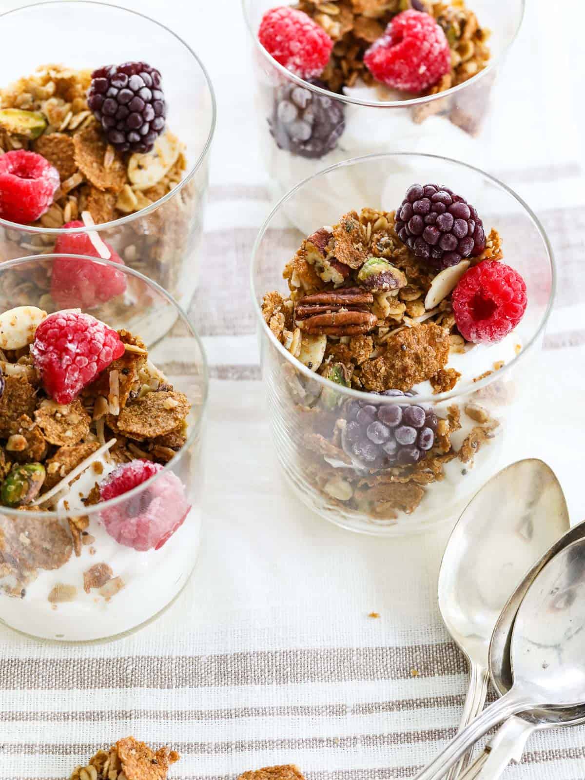 Four yogurt parfaits layered with yogurt, granola, and fresh raspberries and blackberries.