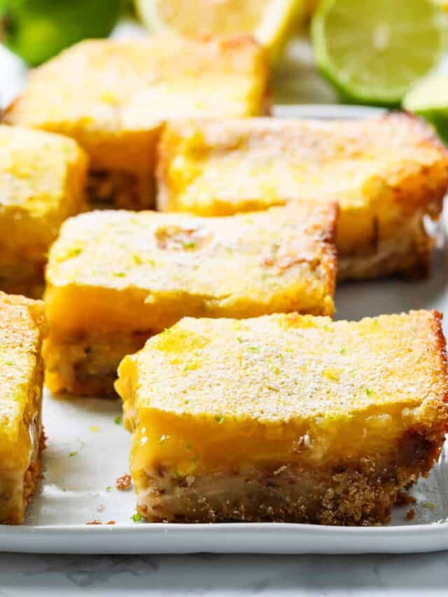 A white platter filled with coconut lime lemon bars topped with powder sugar.