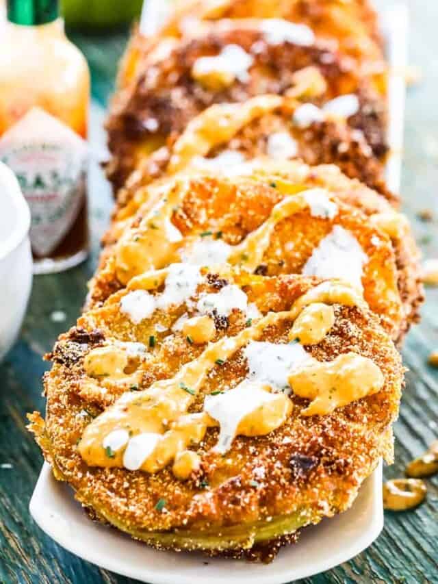 A stack of fried green tomatoes with ranch and remoulade drizzled on top.