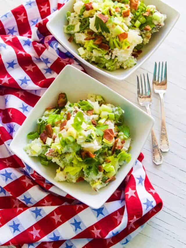 Looking down on to two white square bowls filled with potato salad on a red white and blue star towel and two silver forks.