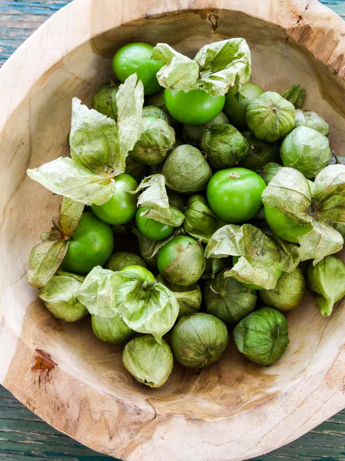 A wood bowl filled with ripe green tomatillos with their husks on.