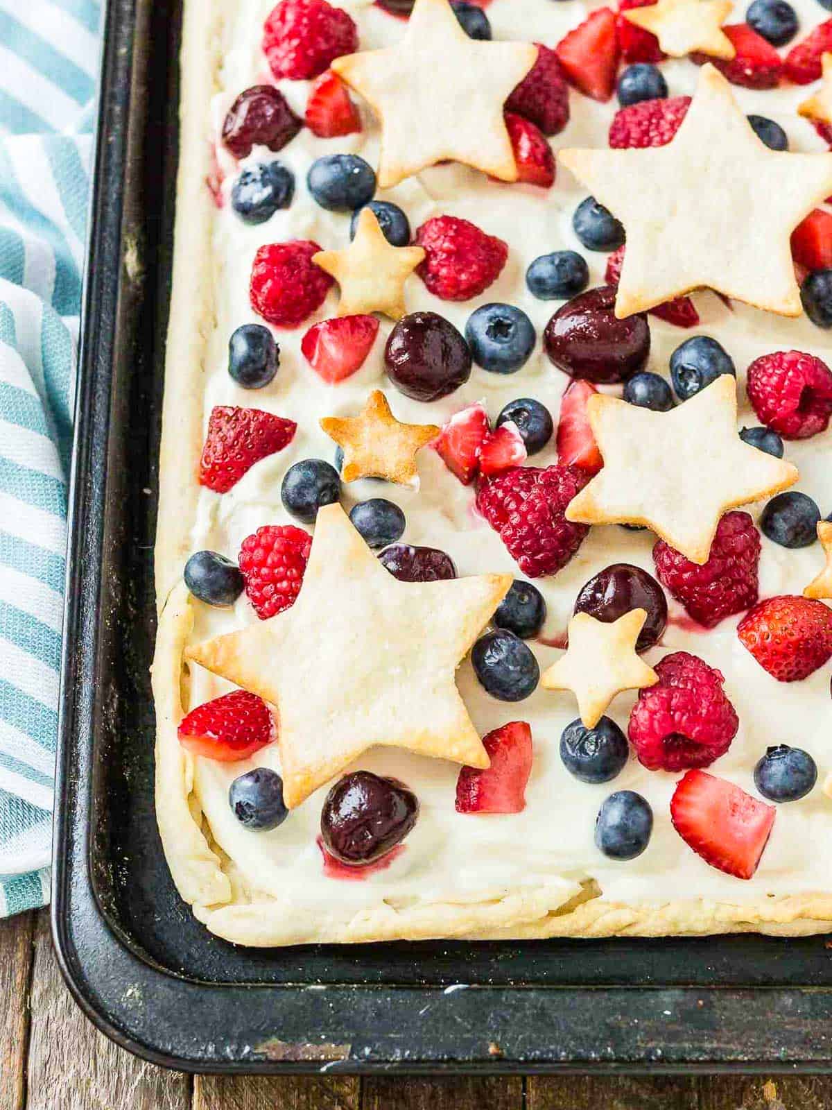 A glass dish holding a berry pie topped with strawberries, blueberries, and pie crust stars.